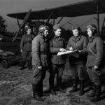 Soviet Night Witches female pilots and crew preparing for a night mission next to a Polikarpov Po-2 bomber. Four pilots are studying a map while a ground crew member pushes a bomb cart.