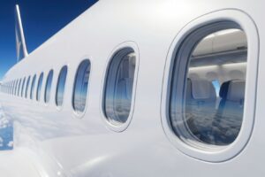 A close-up exterior view of a modern passenger jet featuring round airplane windows, with a blue sky and clouds in the background.